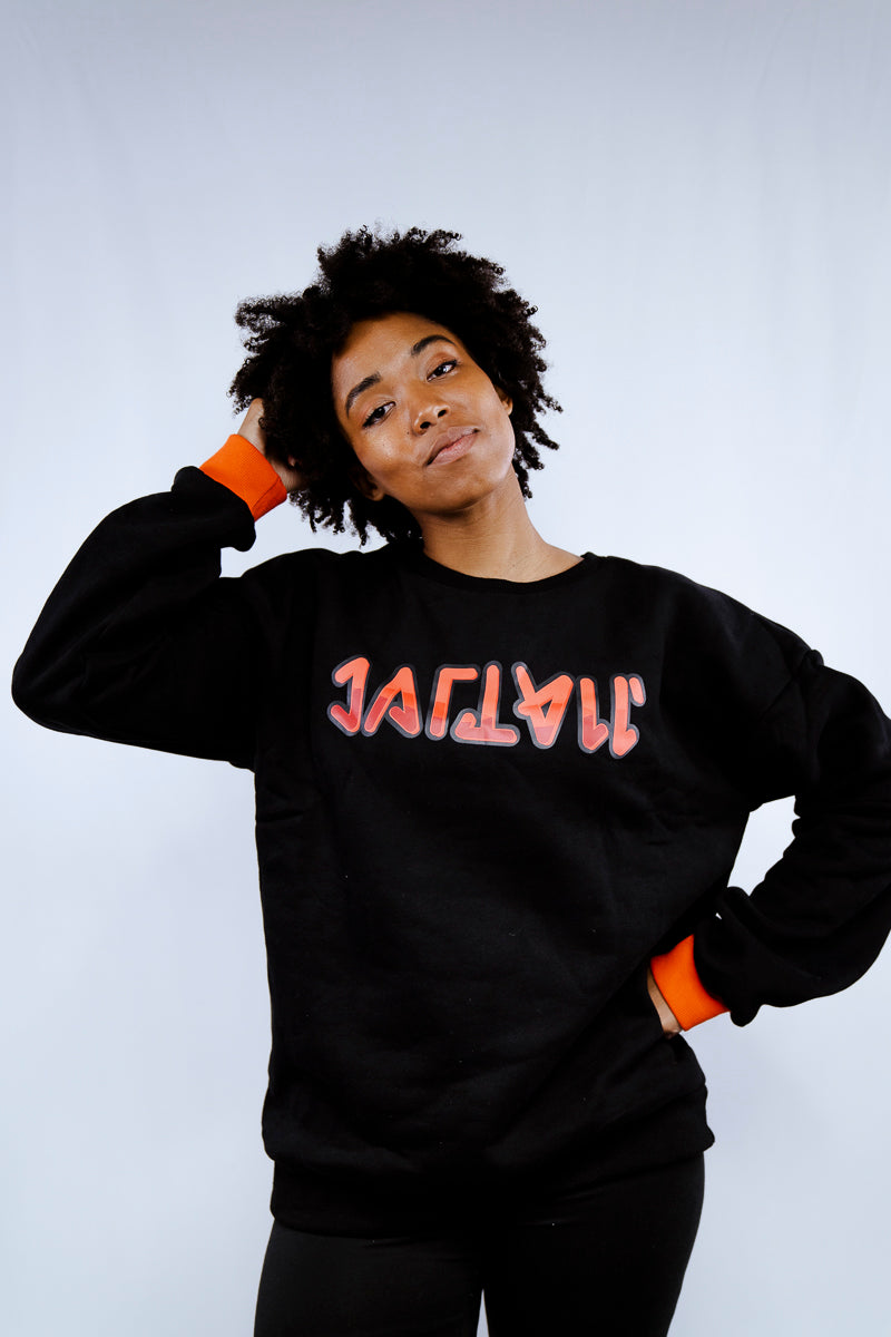 Girl with a hand through her natural hair in a black The Hidden Script  pullover  with red cuffs