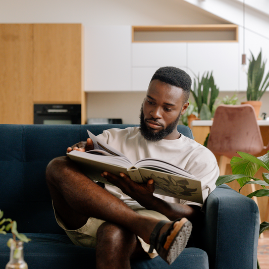 black man guy sitting on couch reading book
